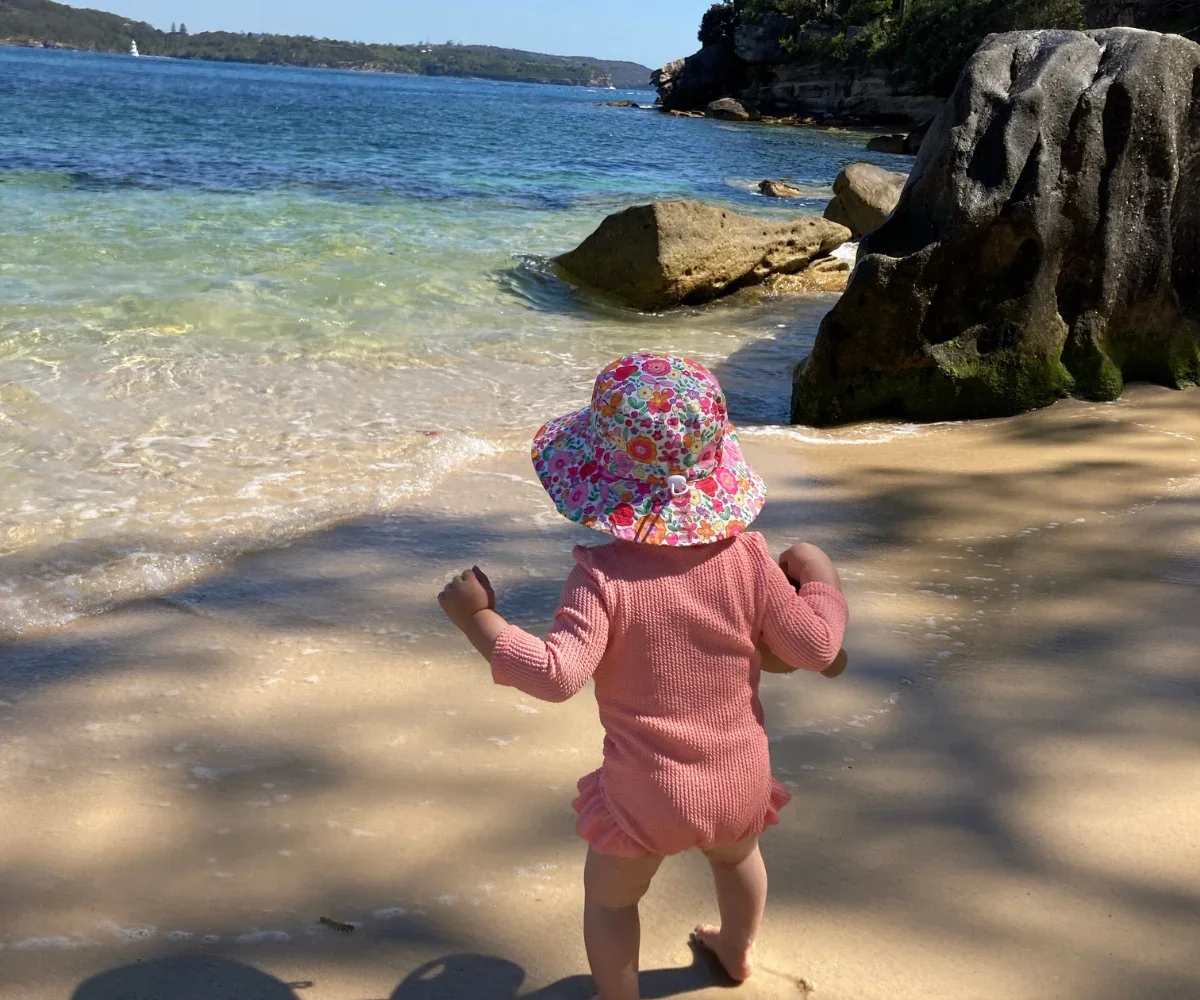 Baby in a floral beach hat walking along the shoreline