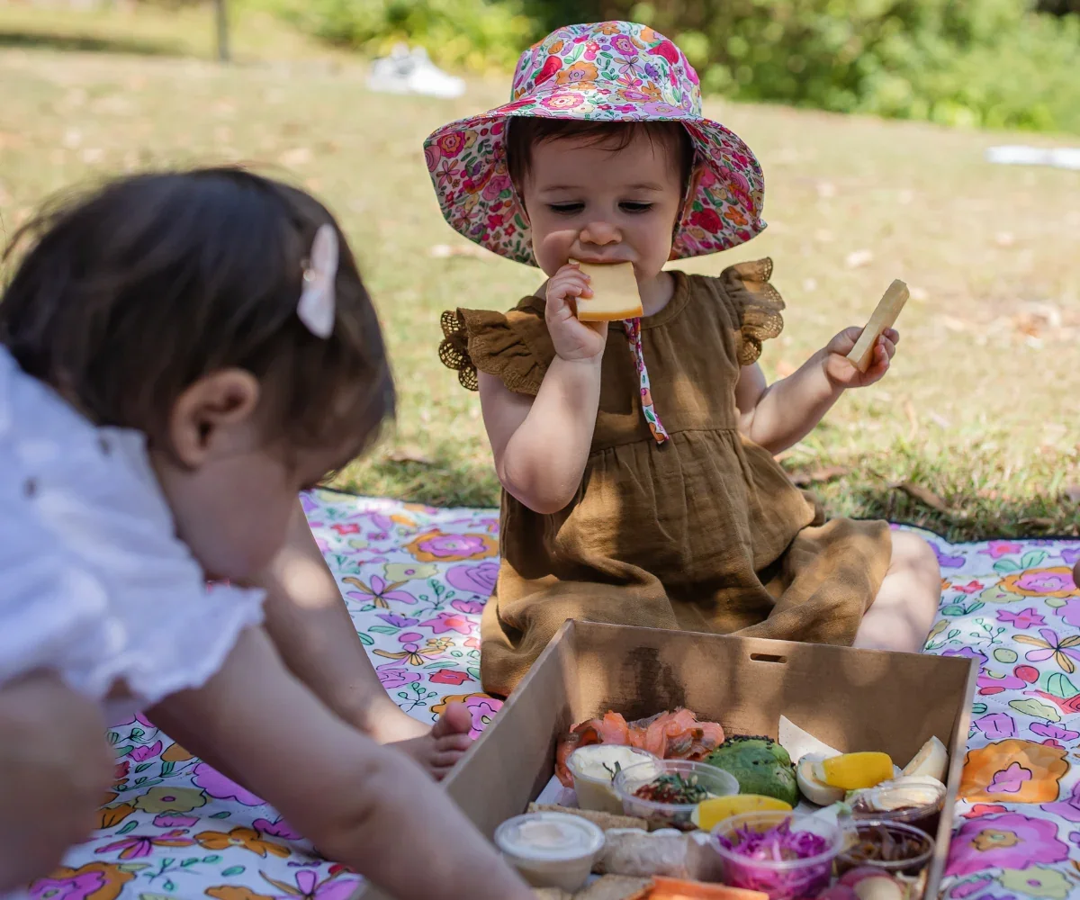 Mum and toddler picnicking on a colourful mat with baby hats