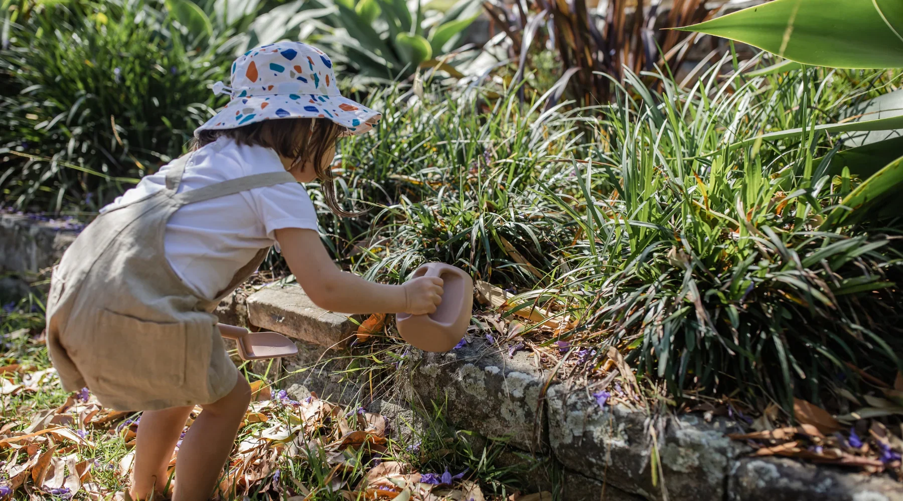 Toddler in a pink sun hat exploring a garden path outdoors