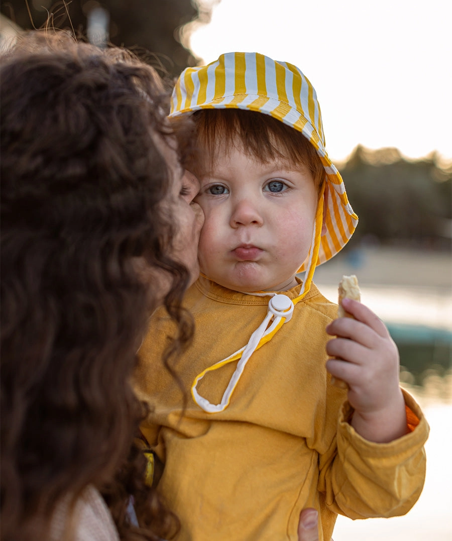 Mum holding her child, who is dressed in a yellow top and beach hat