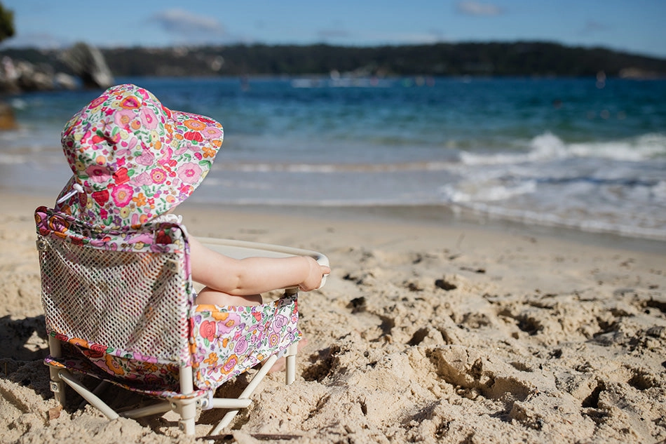 Baby at the beach, sitting in a beach chair and wearing a matching hat