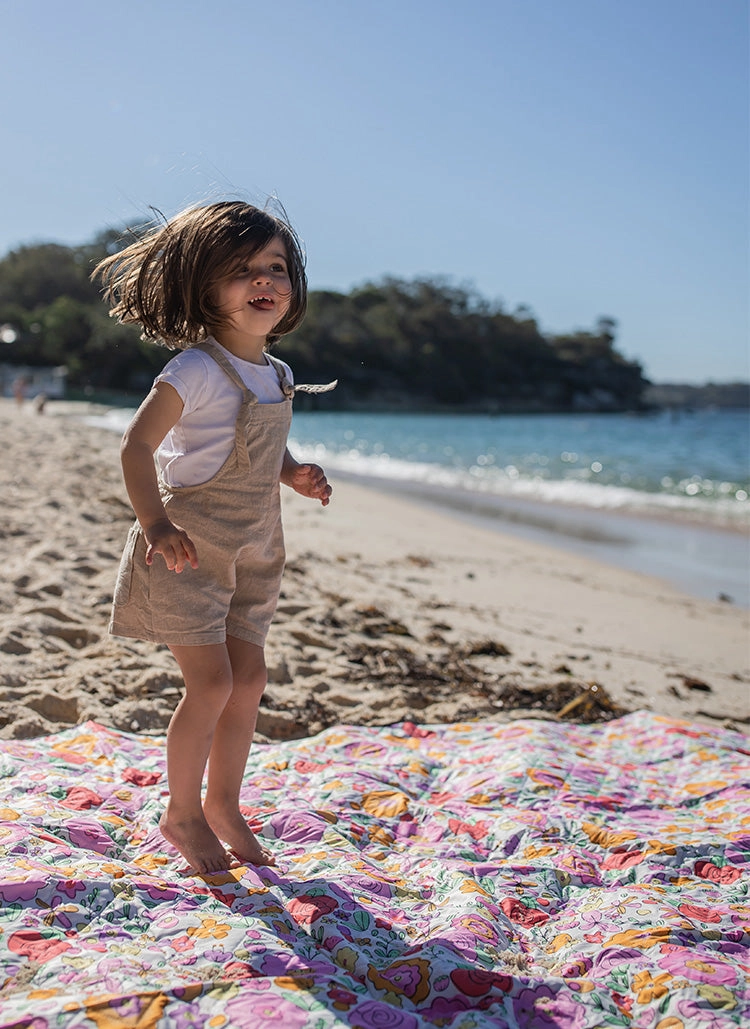 Child at the beach jumping on a colourful picnic mat