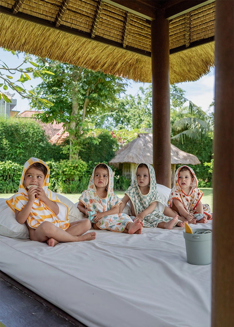 Four children wearing towel ponchos sitting inside a beach cabana