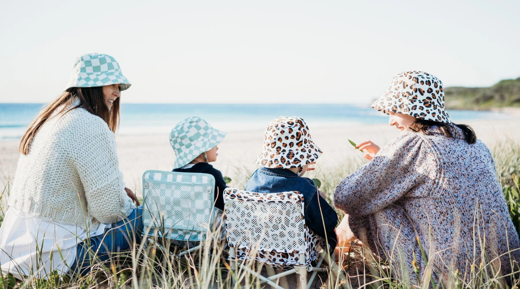 Family sitting on the beach in matching sun hats beside IZIMINI chairs